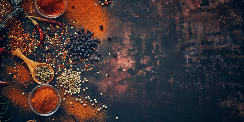 Photo of various spices artfully arranged on a black slate background. The spices include colorful powders, seeds, and herbs, creating a vibrant and visually appealing display.