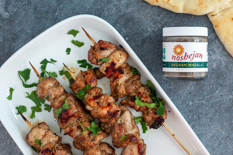 Noshejan Afghan Masala Grilled Chicken Skewers on white rectangle plate and concrete background next to spice jar
