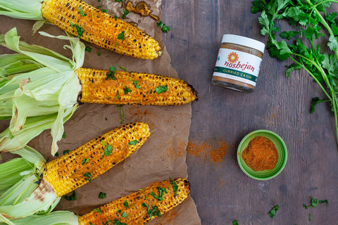 Noshejan Curried Cajun Grilled Corn With Compound Butter on butcher paper on wood background garnished with cilantro.