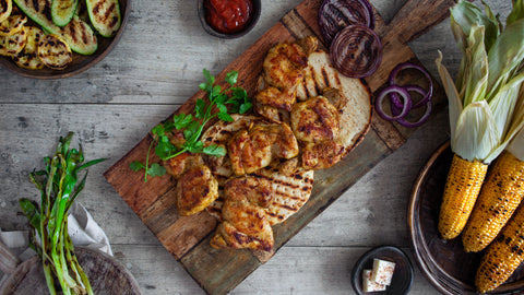 Grilled chicken, onions, zucchini, summer squash, scallions and corn arranged on a cutting board and bowls.